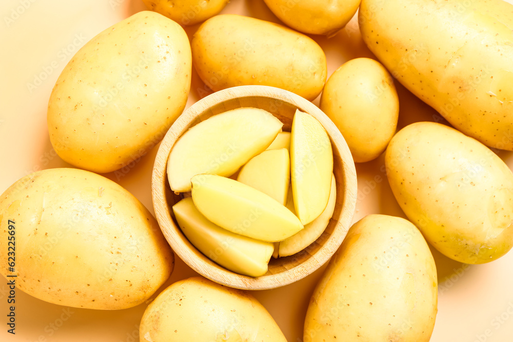 Bowl with cut and whole potatoes on yellow background