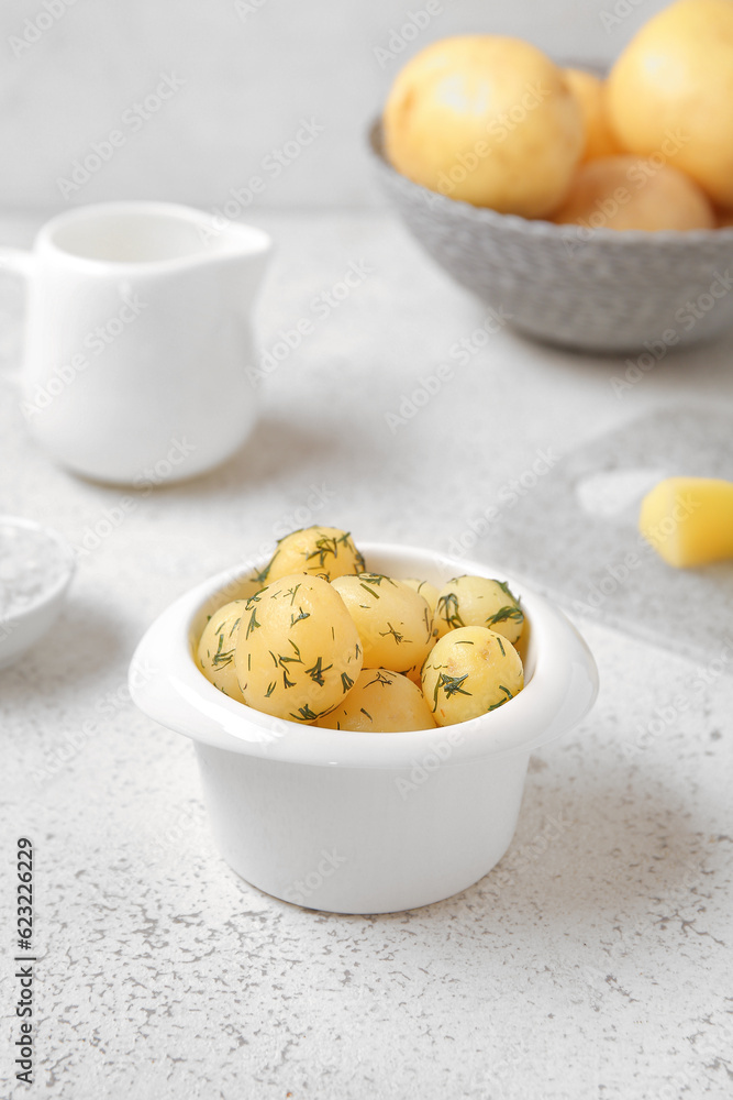 Bowl with boiled baby potatoes on light background