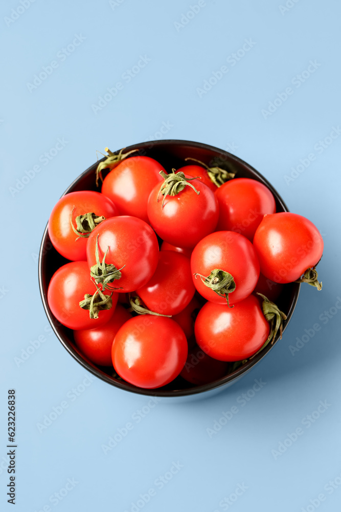 Bowl with fresh cherry tomatoes on blue background