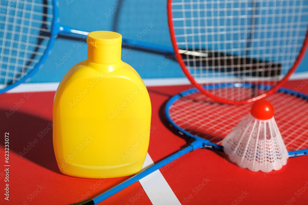 Bottle of sunscreen, badminton rackets and shuttlecock on color background