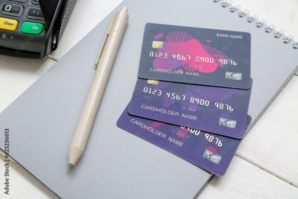 Payment terminal with notebook and credit cards on white wooden background