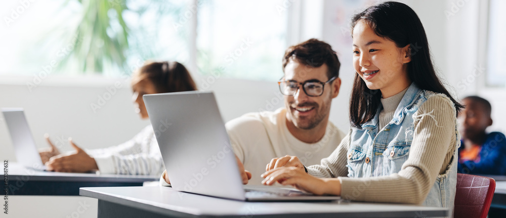 Happy young girl receiving assistance from her teacher in a computer science lesson