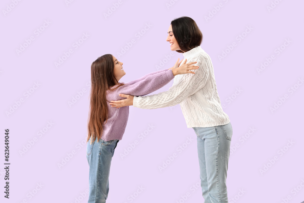 Little girl and her mother in warm sweaters hugging on lilac background