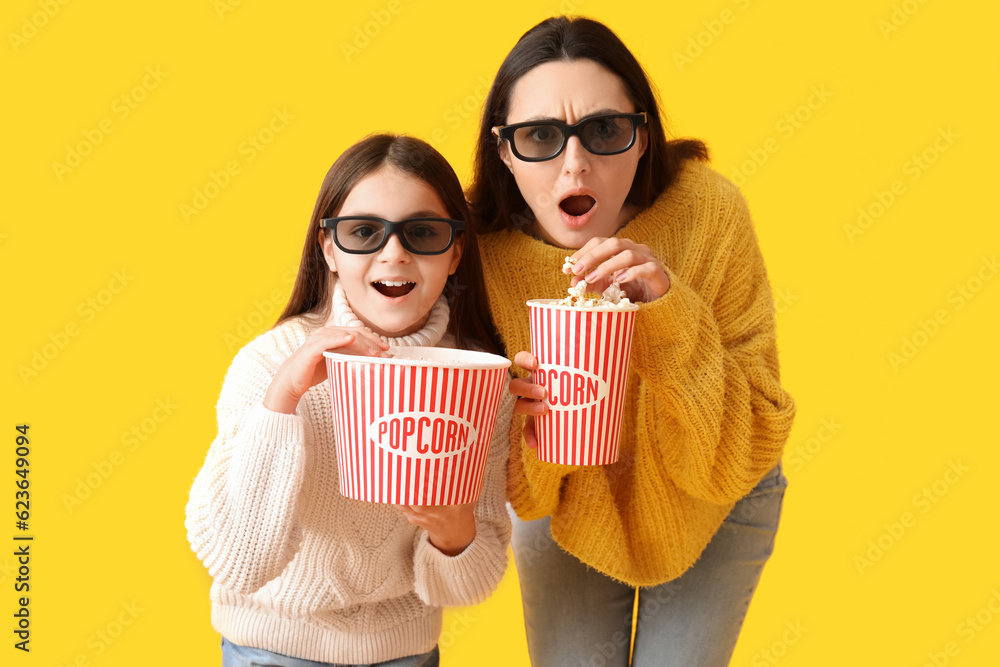 Little girl and her mother in 3D glasses with popcorn on yellow background