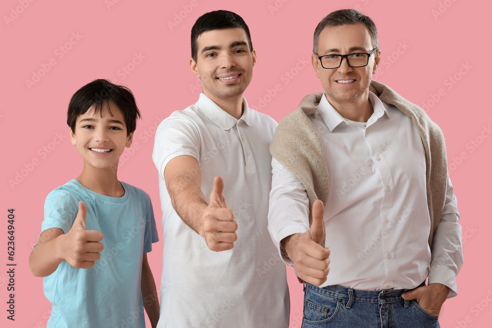 Happy little boy with his dad and grandfather showing thumb-up on pink background