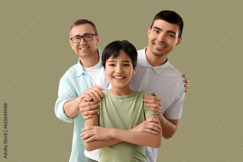 Happy little boy with his dad and grandfather hugging on green background