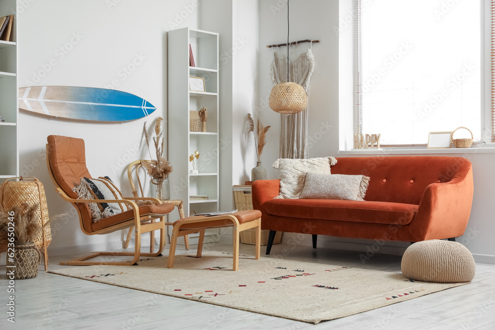 Interior of light living room with surfboard, brown sofa and armchair