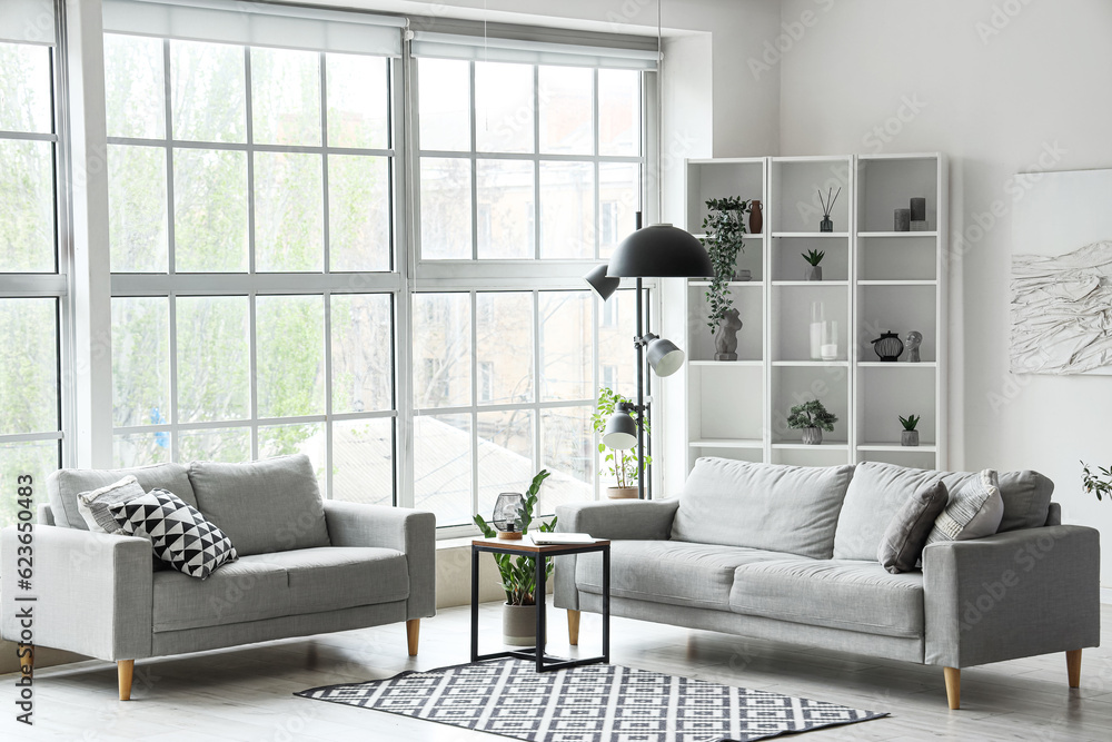 Interior of light living room with grey sofas, modern laptop on coffee table and big window