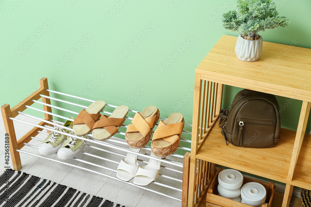 Shelving unit and stand with shoes near green wall in hall