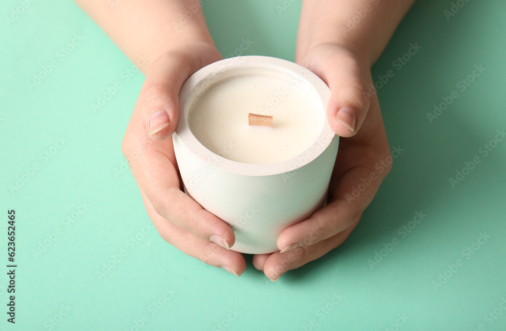 Female hands holding candle on turquoise background