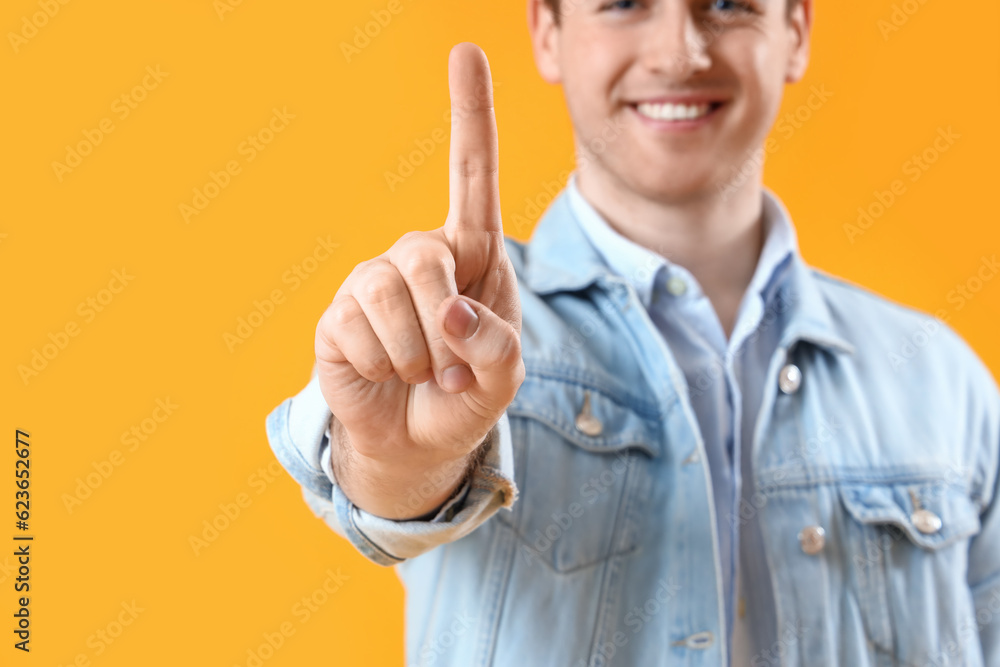 Young man using virtual screen on yellow background, closeup