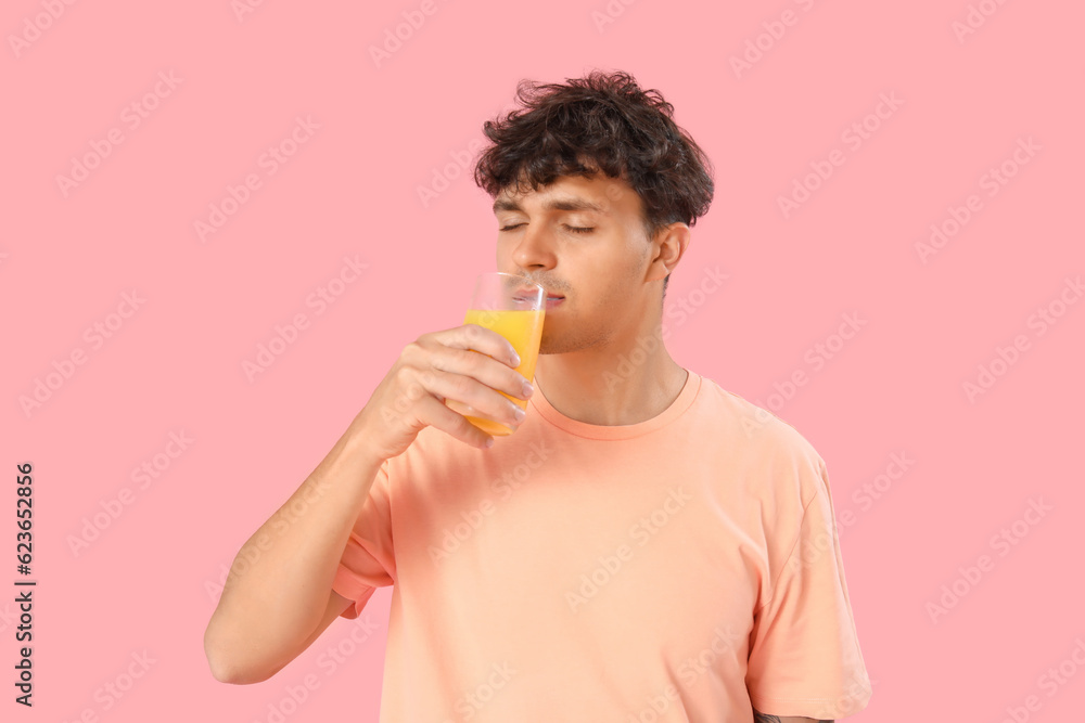 Young man with glass of orange juice on pink background