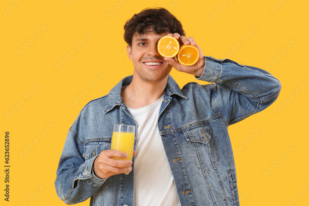 Young man with oranges and glass of juice on yellow background