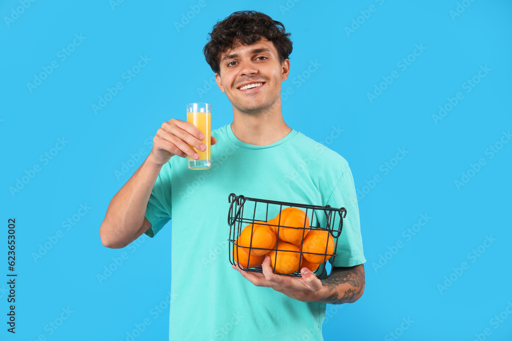 Young man with oranges and glass of juice on blue background