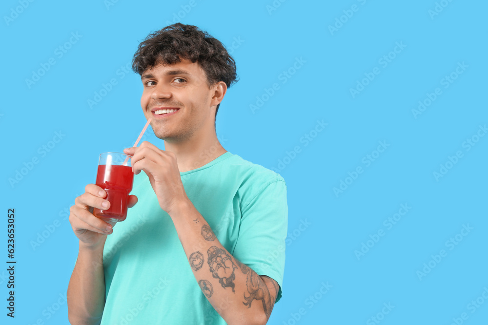 Young man with glass of red juice on blue background