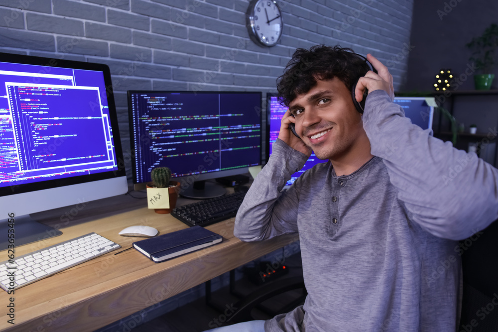 Male programmer working with headphones and computer in office at night