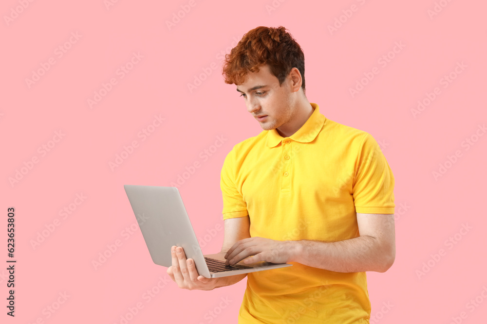 Male programmer working with laptop on pink background