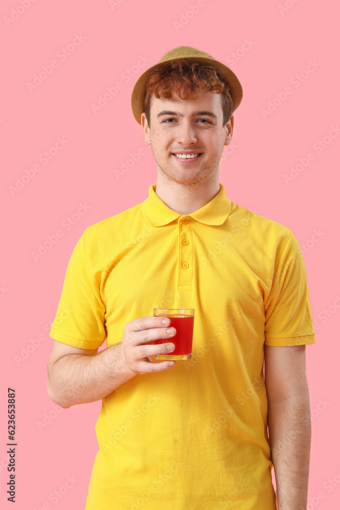 Young man with glass of red juice on pink background