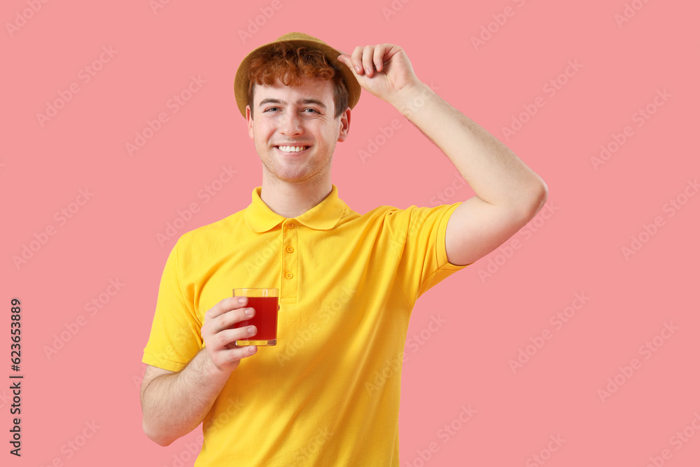 Young man with glass of red juice on pink background