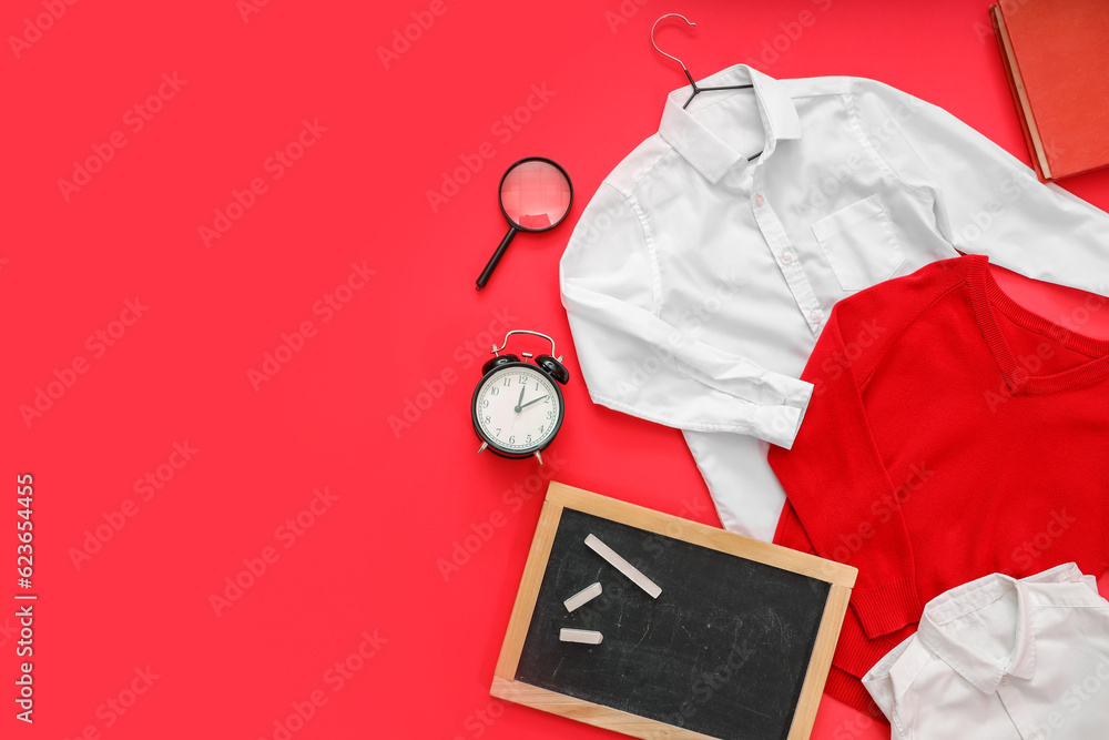 Composition with stylish school uniform, chalkboard, alarm clock and stationery on red background