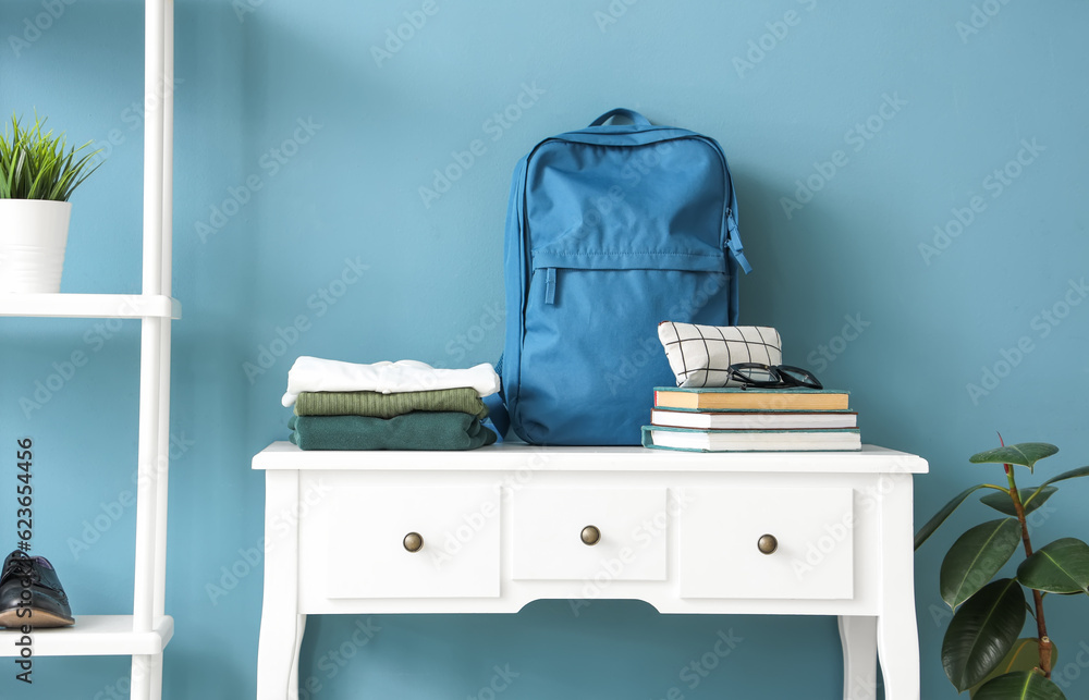 Table with stylish school uniform, backpack, books and shelving unit near blue wall in room