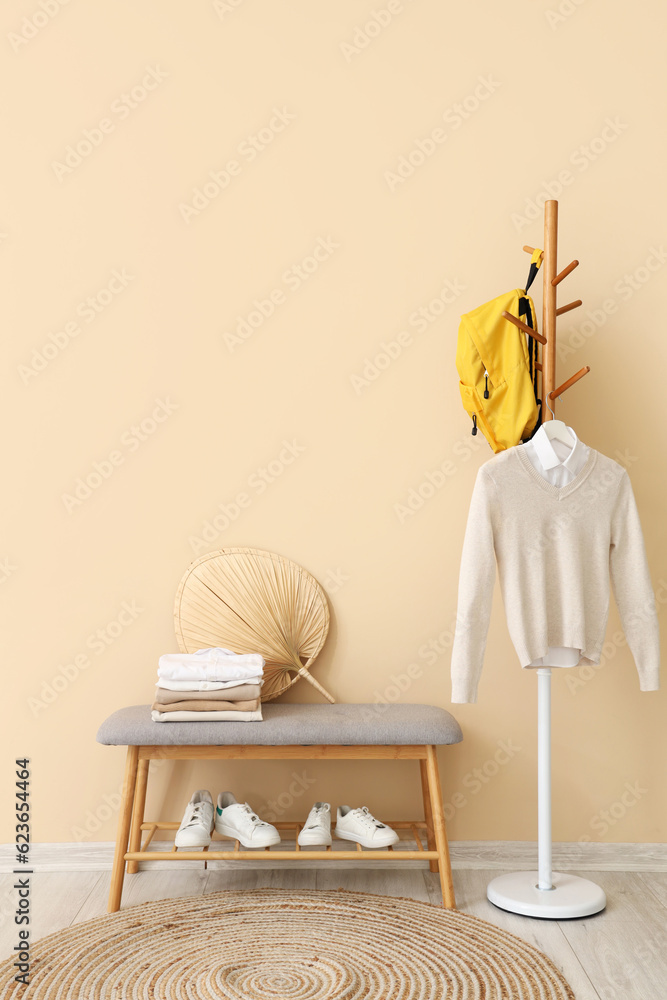 Stylish school cardigan with shirt, backpack hanging on rack, bench and sneakers near beige wall in 