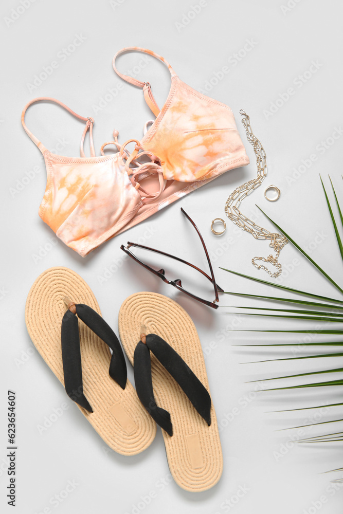 Stylish bikini top, flip-flops, sunglasses, accessories and palm leaf on light background