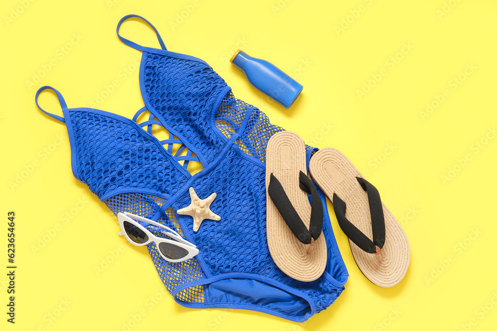 Stylish swimsuit, flip-flops, sunglasses and bottle of sunscreen cream on yellow background