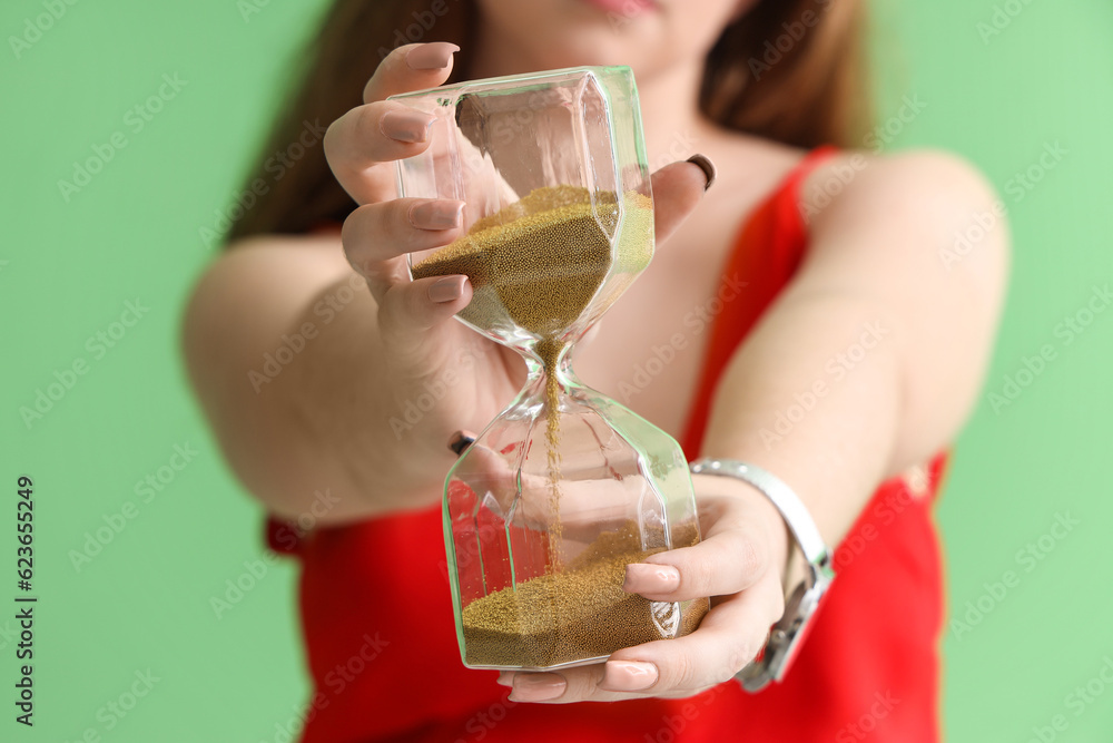 Young woman with hourglass on green background, closeup. Deadline concept