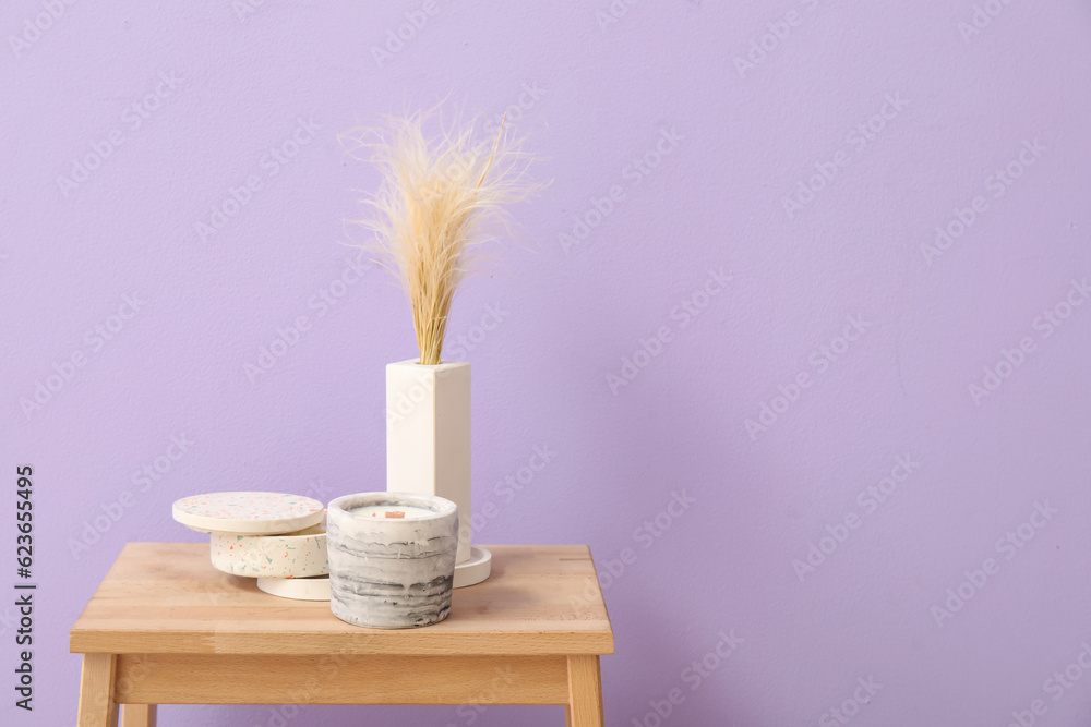 Holders with candles and pampas grass on wooden table near purple wall in room