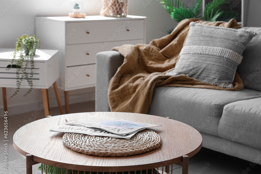 Wooden coffee table with wicker mat and magazines near sofa in light living room