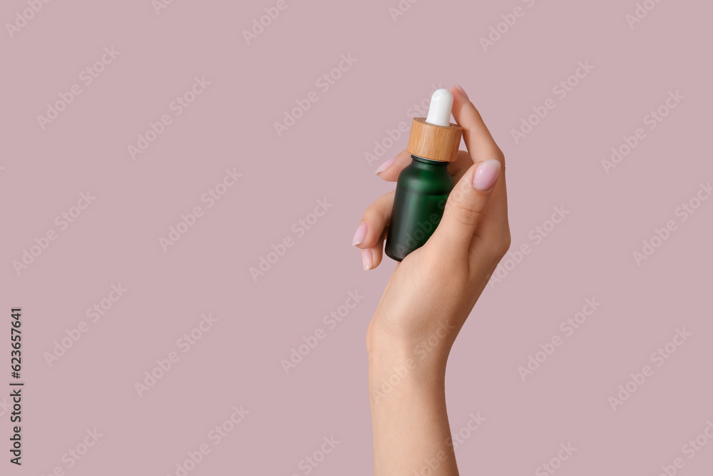 Hand of woman with bottle of cosmetic oil on pink background