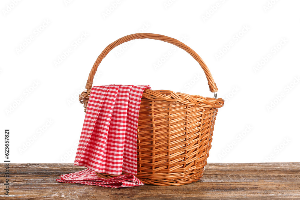 Wicker picnic basket and red checkered napkin on wooden table against white background