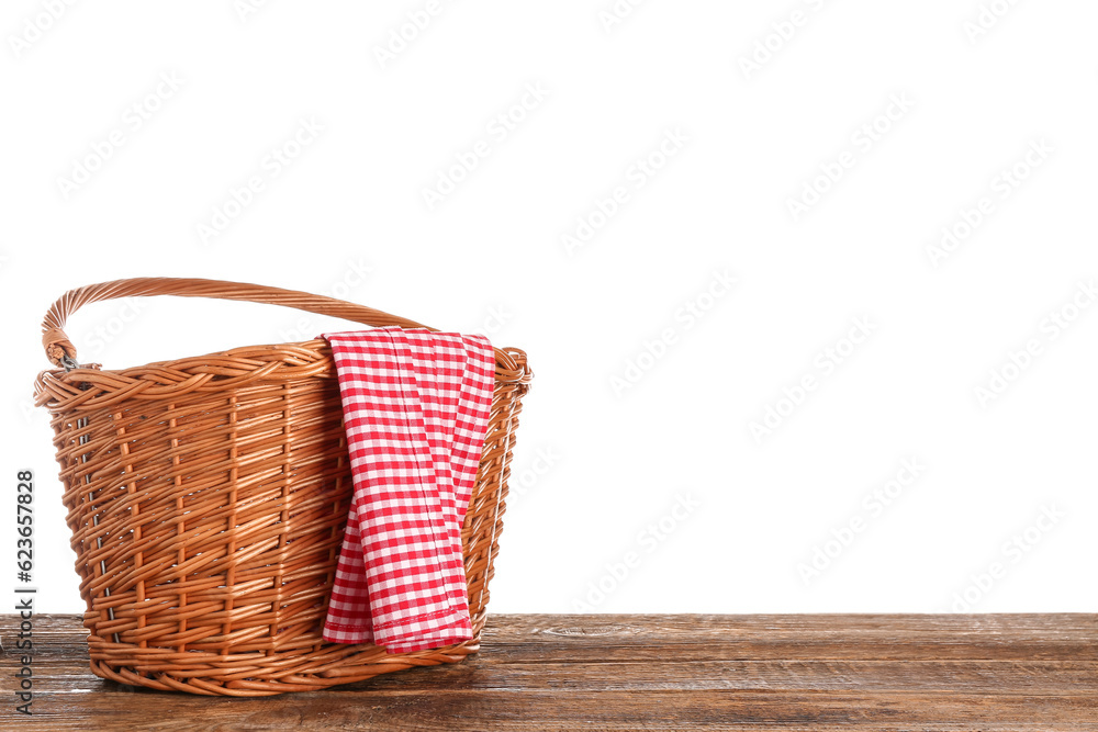 Wicker picnic basket and red checkered napkin on wooden table against white background