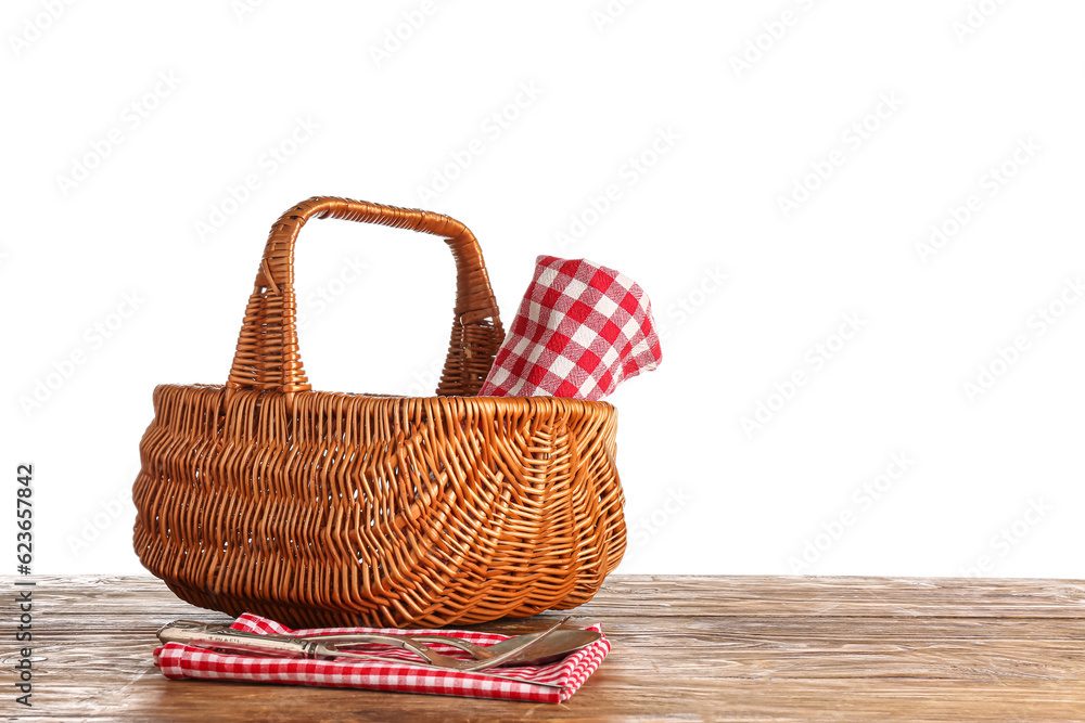 Wicker picnic basket with napkin and cutlery on wooden table against white background