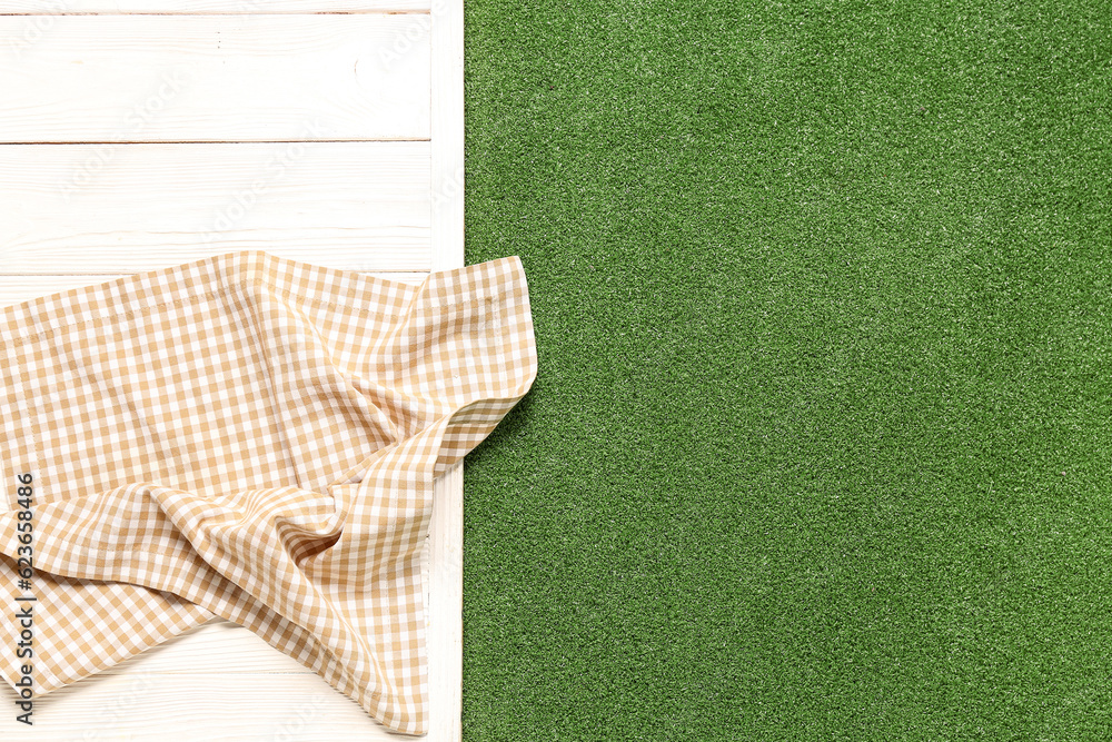 Clean napkin on light wooden table against green grass background