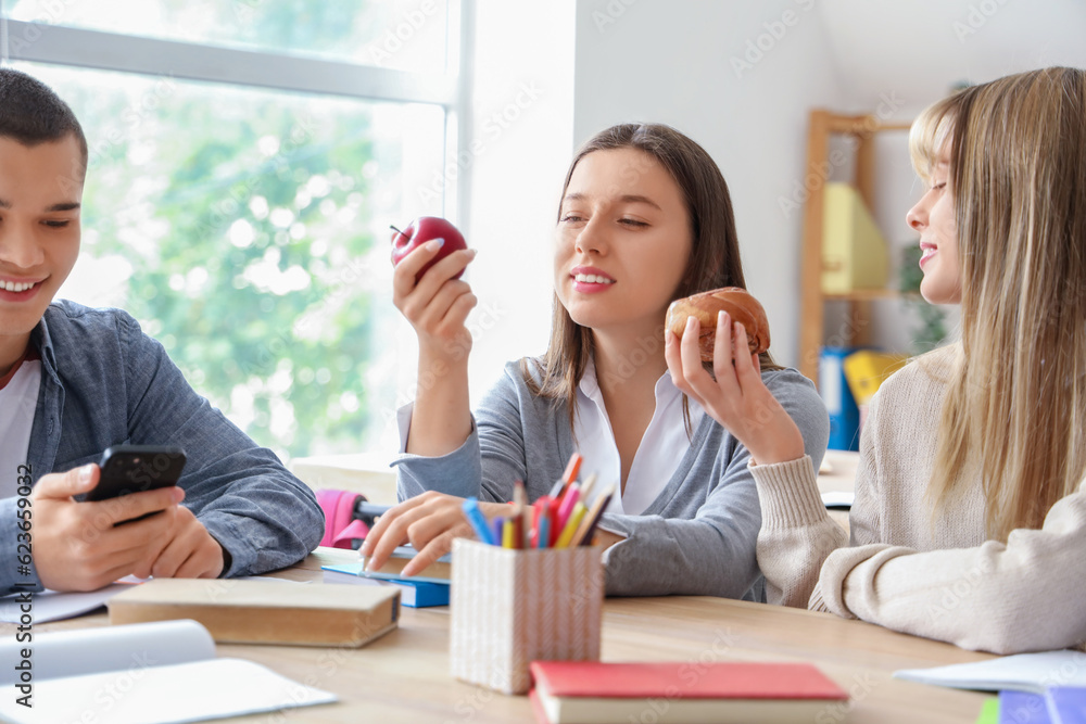 Group of teenage students having snacks at table in classroom