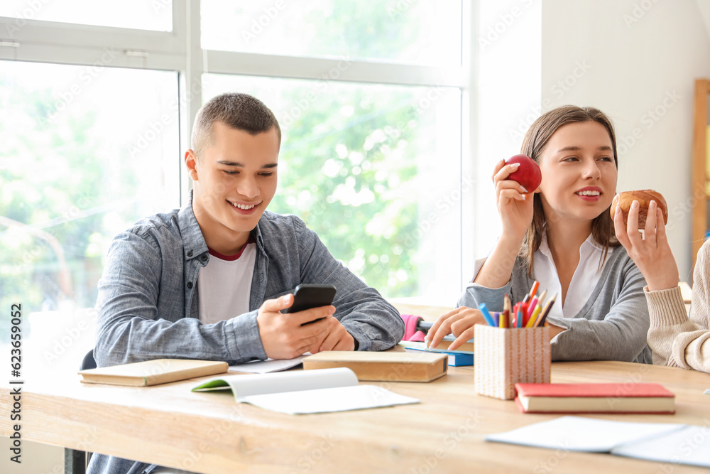 Male student using mobile phone at table in classroom