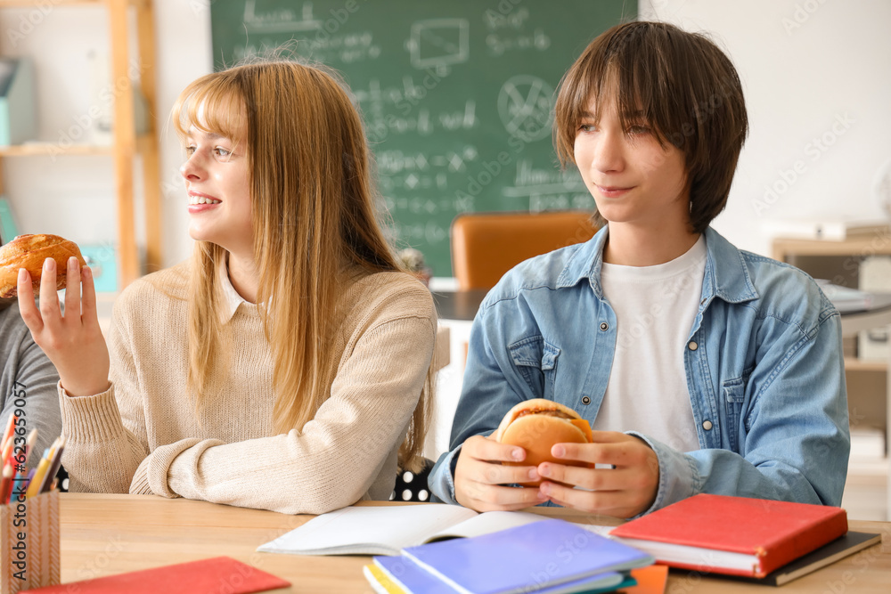 Teenage students having snacks at table in classroom