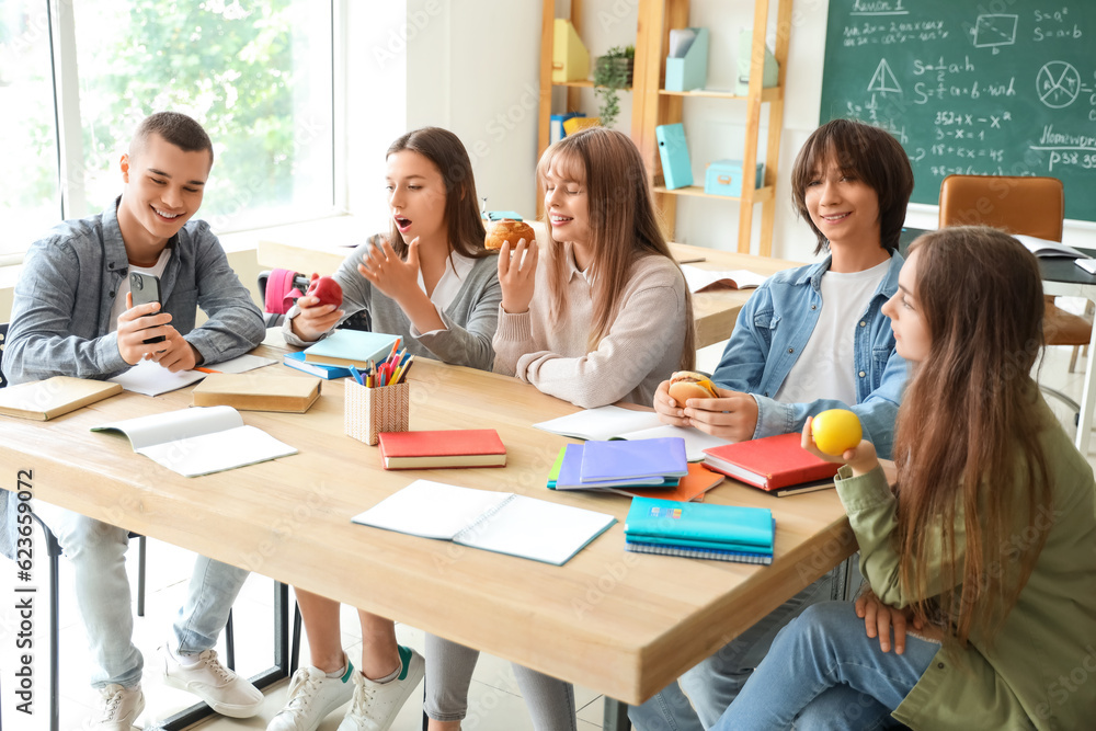 Group of teenage students having snacks at table in classroom