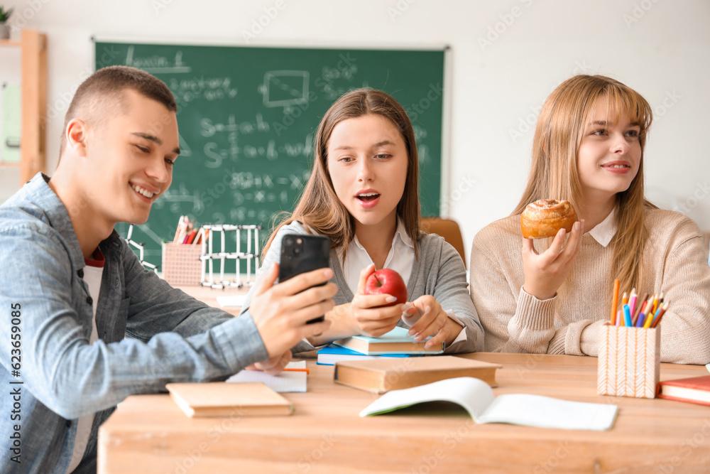 Group of teenage students having snacks at table in classroom