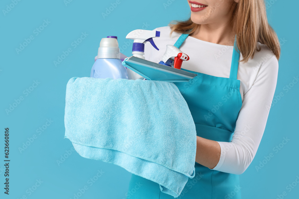 Young woman with cleaning supplies on blue background, closeup