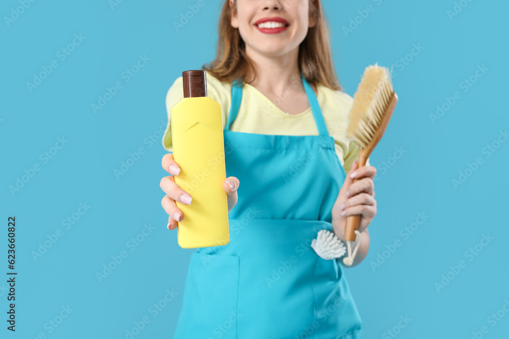 Young woman with bottle of detergent and cleaning brush on blue background, closeup