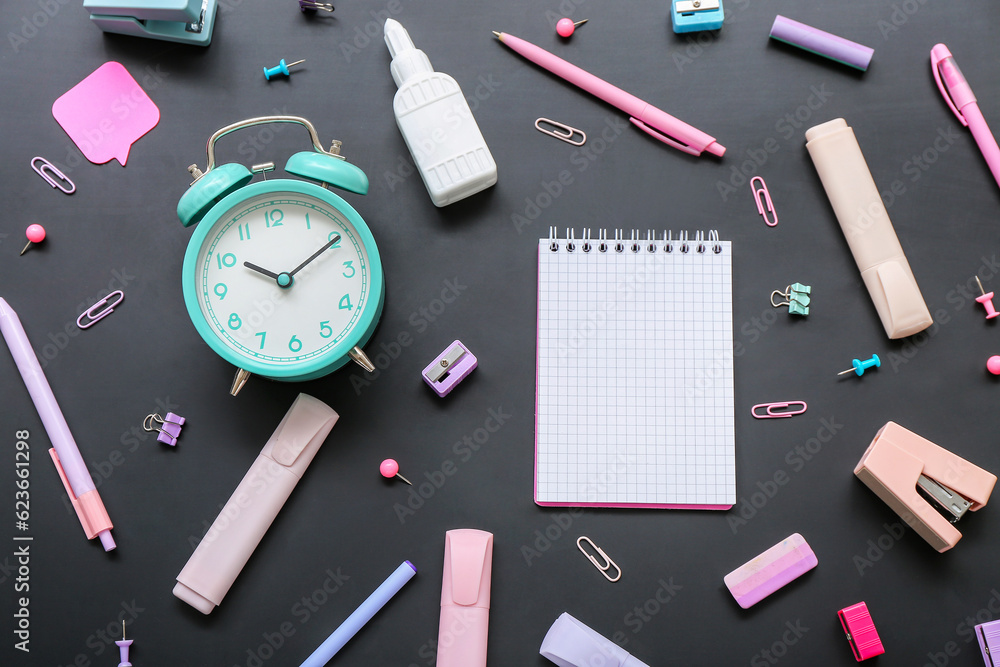 Blank notebook with alarm clock and stationery on black chalkboard