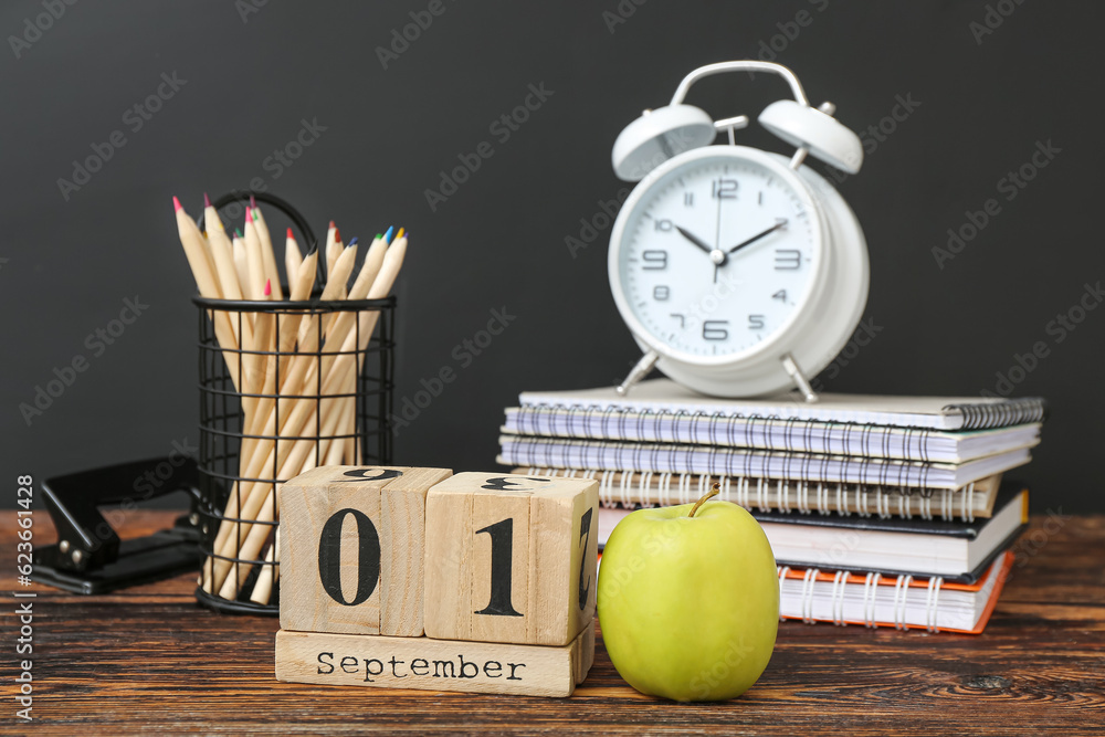 Different stationery, alarm clock and calendar with date SEPTEMBER 1 on wooden table against black c