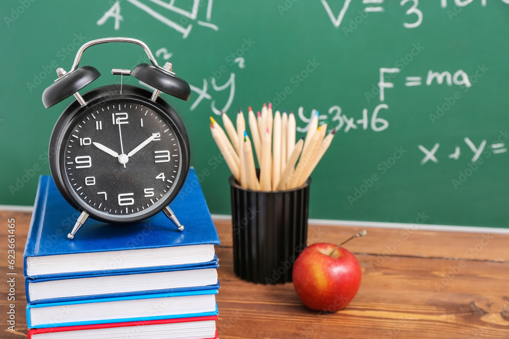 Stationery, alarm clock and fresh apple on wooden table against green chalkboard with formulas