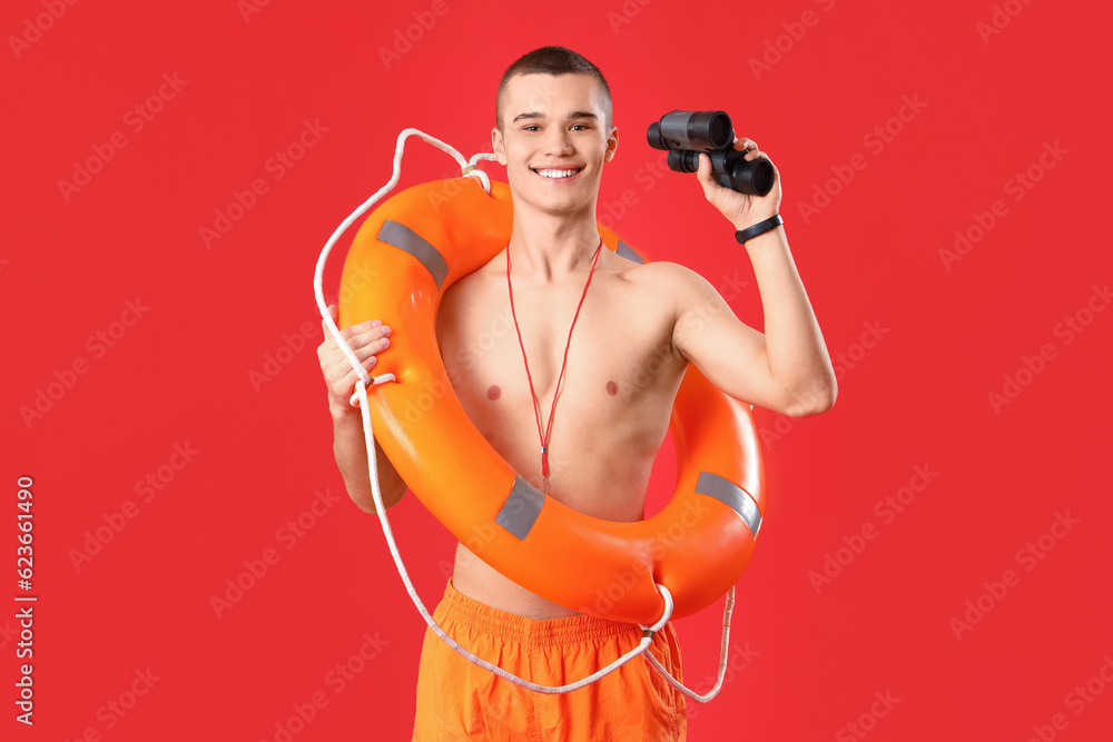 Male lifeguard with binoculars and ring buoy on red background