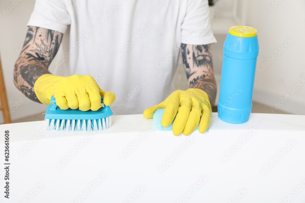 Young tattooed man cleaning bathtub in bathroom