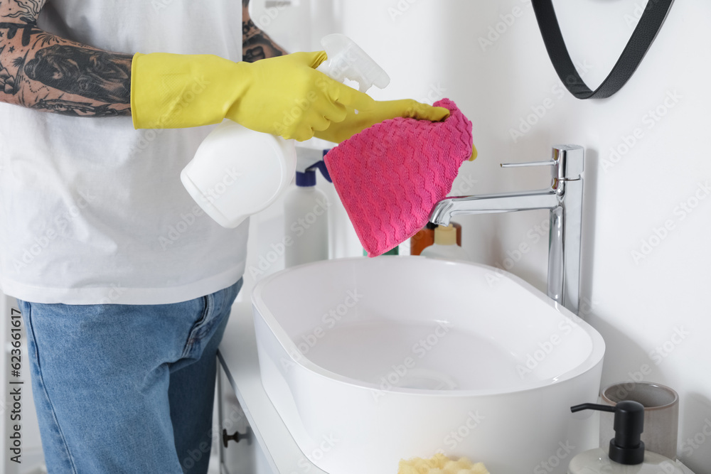 Young tattooed man cleaning sink in bathroom, closeup