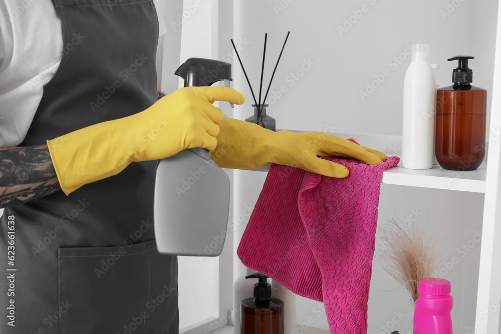 Young tattooed man cleaning shelf in bathroom, closeup